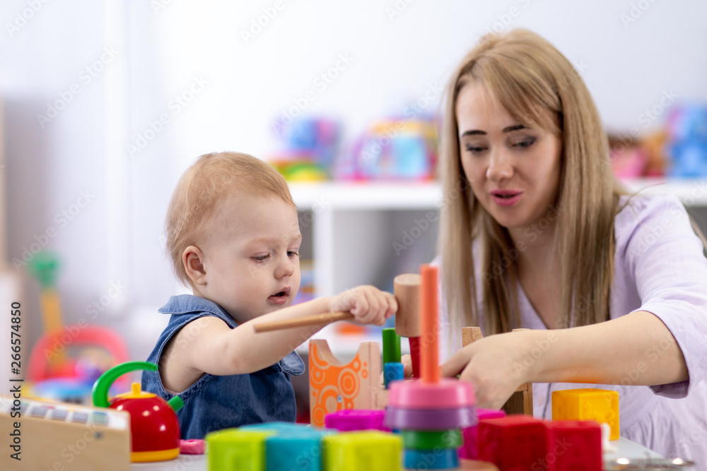 Baby plays with mother or teacher in nursery or day care centre