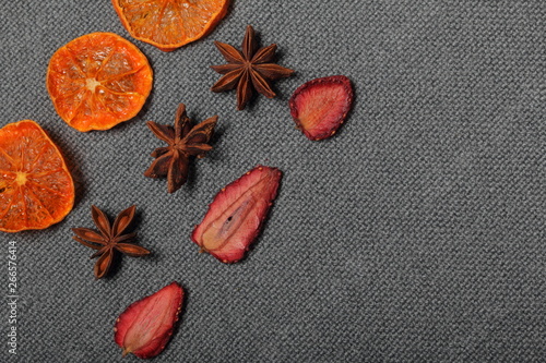 Fototapeta Naklejka Na Ścianę i Meble -  Tangerines are cut into slices and dried to decorate desserts. Nearby are stars of anise and strawberry slices. On a gray background.