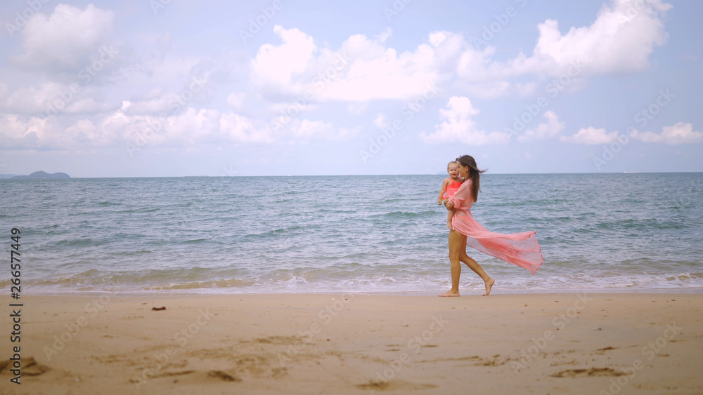 mom and little daughter walk along the shore of a beautiful blue sea, the concept of leisure, family.