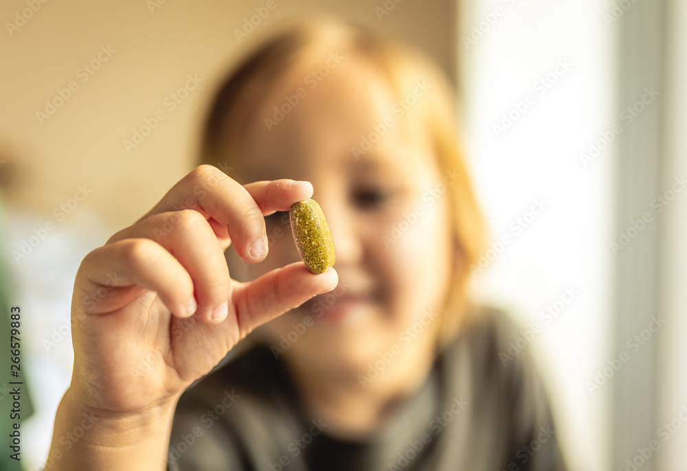 Young boy stares at vitamin or prescription pill that he his holding in hand. Health care or addiction concept. Young boy stares at vitamin or prescription pill that he his holding in hand. Health care or addiction concept.