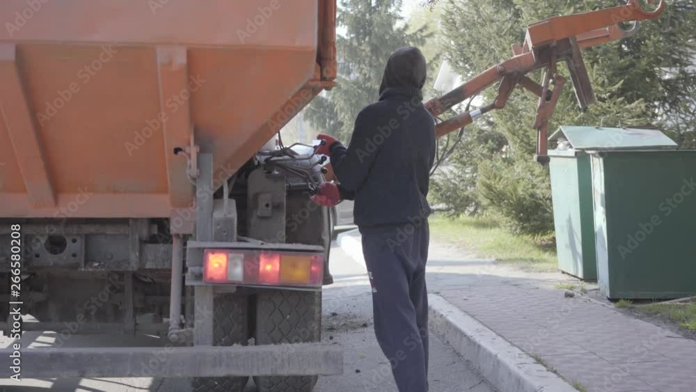 Back view of the man controlling garbage machine work. The worker in casual clothes puts on dumpster using trash machine Back view of the man controlling garbage machine work. The worker in casual clothes puts on dumpster using trash machine