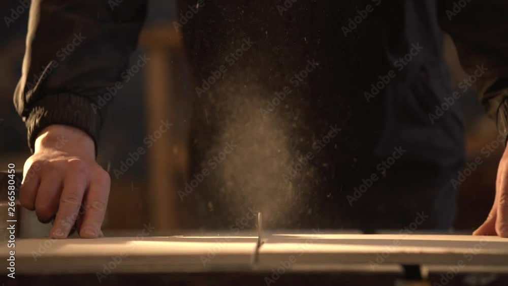 Medium shot side view of mature furniture maker using circular saw to make cuts in wooden plank in workshop light with sunlight Medium shot side view of mature furniture maker using circular saw to make cuts in wooden plank in workshop light with sunlight