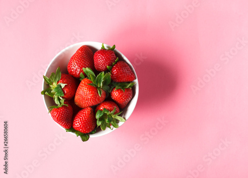 Strawberries in bowls on pink background, top view.