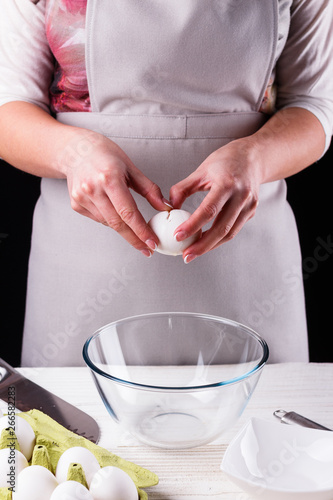 young woman in a gray aprons breaks the eggs