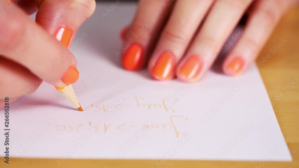 woman is holding an orange pencil and makes notes on a white paper woman is holding an orange pencil and makes notes on a white paper