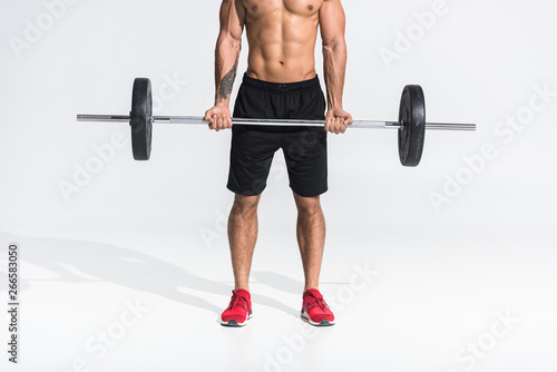 cropped view of mixed race man in black shorts and red sneakers holding barbell on white