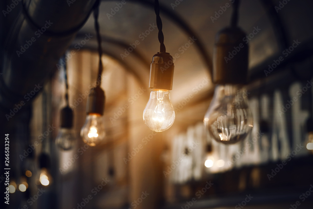 Glass light bulbs hanging on the wires on the roof near the cafe, glow brightly in the darkness of the night Glass light bulbs hanging on the wires on the roof near the cafe, glow brightly in the darkness of the night