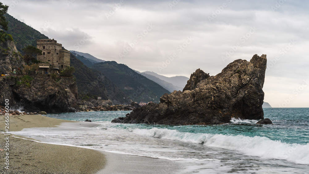 The iconic Rock of Monterosso al Mare in the foamy morning tide washing the beach of the lovely village, on a rainy day in Cinque Terre, Italy.