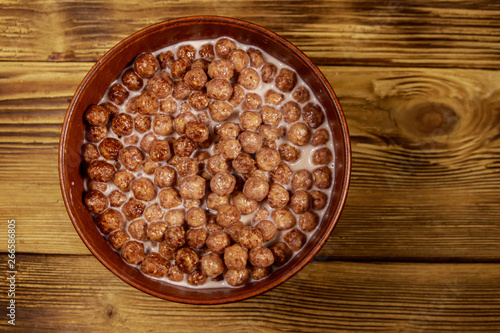 Cereal chocolate balls with milk in a bowl on wooden table. Top view