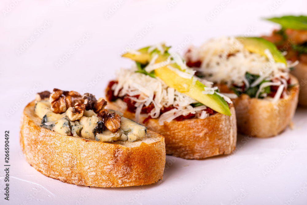 Brushetta set for an aperitif. Variety of small sandwiches with tomatoes, parmesan cheese, avocado and walnut served on a white background