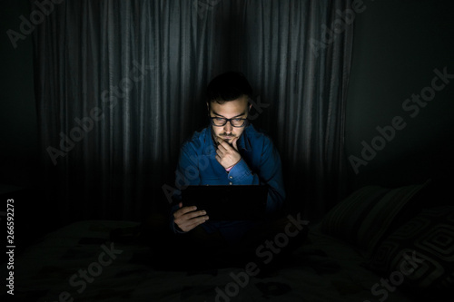 Man watching tv series in a tablet sitting on a bed in the night at home
