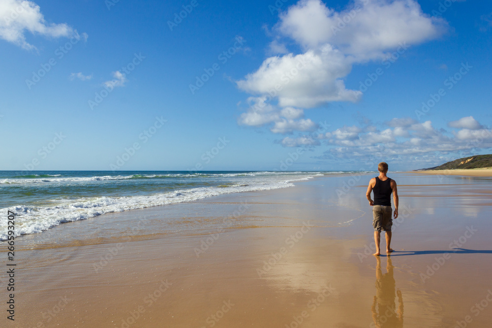 young man walking on the ain transportation highway on Fraser Island - wide wet sand beach coast facing Pacific ocean - long 75 miles beach