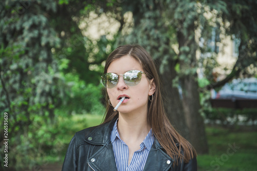portrait of a beautiful young woman in the park with a cigarette in her mouth
