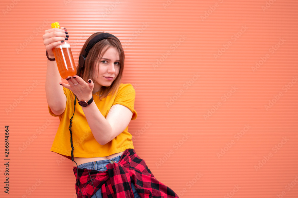 a young beautiful girl is standing on an orange background, holding a plastic bottle of beer a young beautiful girl is standing on an orange background, holding a plastic bottle of beer