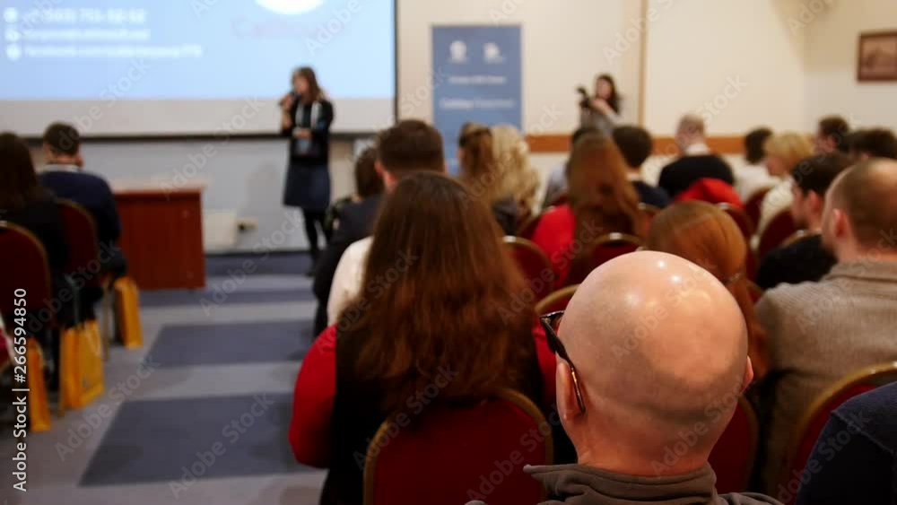 A business conference. People sitting on the chairs and looking at presentation screen in the hall A business conference. People sitting on the chairs and looking at presentation screen in the hall