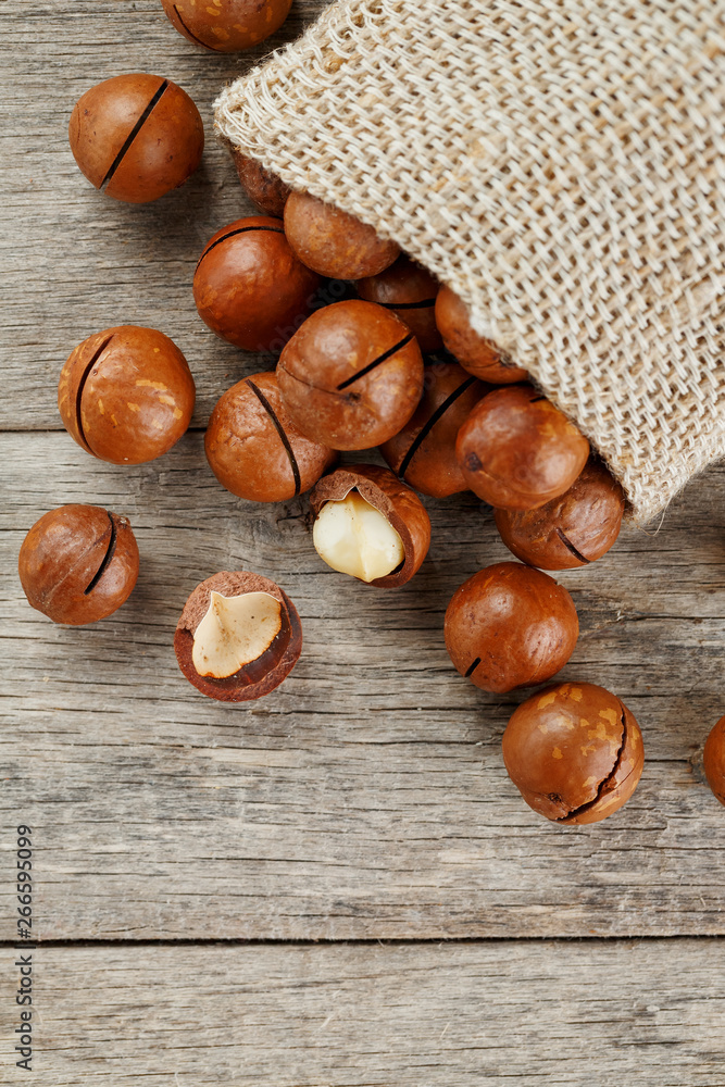 Macadamia nuts spilled out of the bag on a wooden background close-up with one peeled nut Macadamia nuts spilled out of the bag on a wooden background close-up with one peeled nut