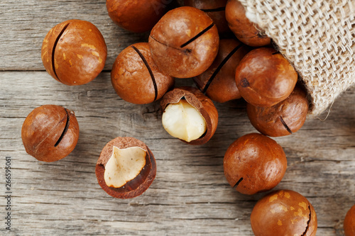 Macadamia nuts spilled out of the bag on a wooden background close-up with one peeled nut