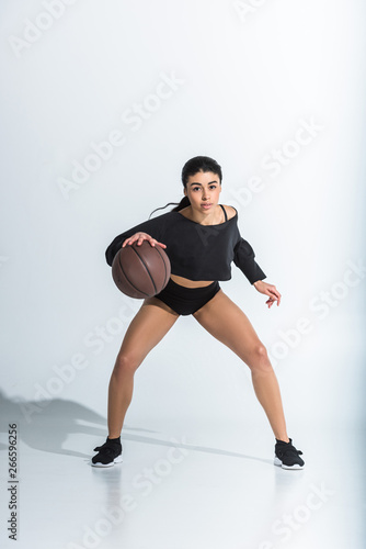 attractive sportive african american girl playing ball and looking at camera on white