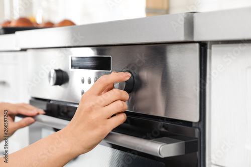 Woman regulating cooking mode on oven panel in kitchen, closeup