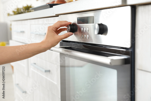 Woman regulating cooking mode on oven panel in kitchen, closeup