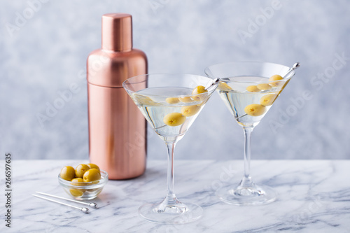 Martini cocktail with green olives, shaker on marble table background. Copy space.