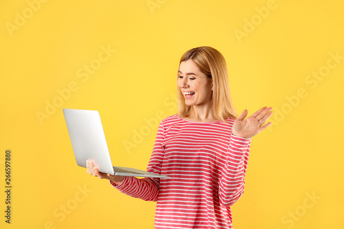 Woman using laptop for video chat on color background