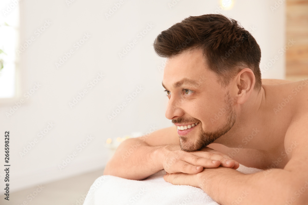 Obraz premium Handsome man relaxing on massage table in spa salon, space for text
