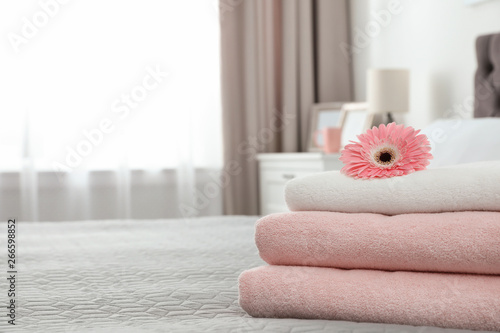 Stack of clean towels with flower on bed indoors. Space for text