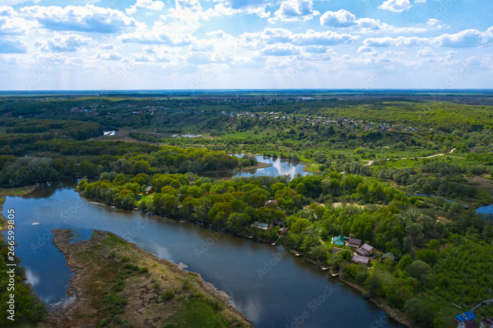 Aerial view of river with reflected blue sky and clouds, green meadows with trees and plants. Beautiful summer nature landscape from above