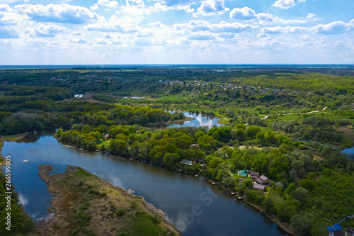Aerial view of river with reflected blue sky and clouds, green meadows with trees and plants. Beautiful summer nature landscape from above