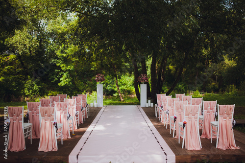 Beautiful setting for outdoors wedding ceremony. Chairs for guests of the bride and groom are decorated in the same style, decorated with fashionable fabric.  chairs are placed convolution with  rose  © SergeVo