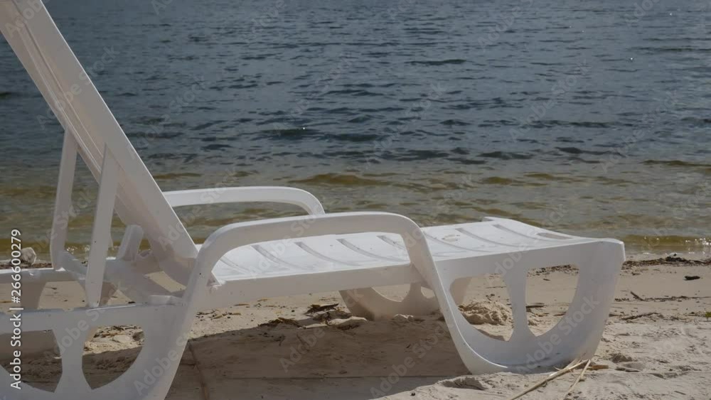 White lounge chairs are beautifully furnished facing the river.Empty chaise lounge on the river beach. White sun loungers on the beach.Weekend at the river White lounge chairs are beautifully furnished facing the river.Empty chaise lounge on the river beach. White sun loungers on the beach.Weekend at the river