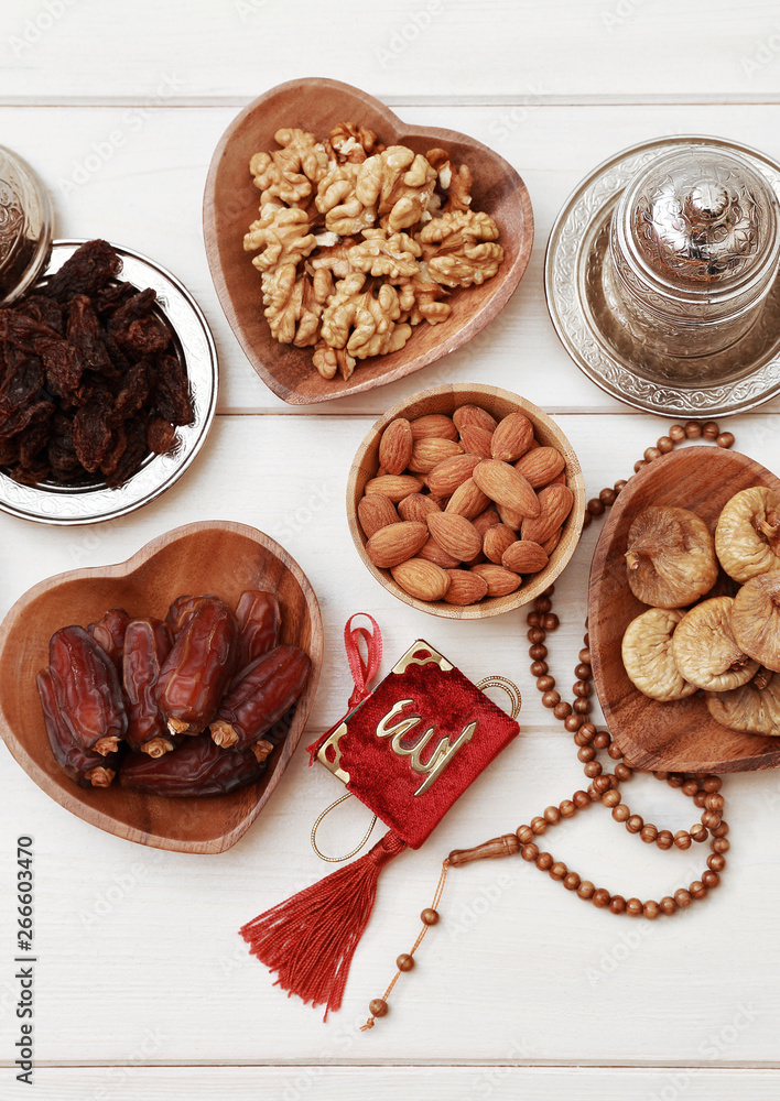 Ramadan iftar party concept. Islamic holy book Quran and rosary beads with delicious dates, dried figs, dried apricots, walnuts, almonds, raisins on bamboo plates on a white wooden table background. Ramadan iftar party concept. Islamic holy book Quran and rosary beads with delicious dates, dried figs, dried apricots, walnuts, almonds, raisins on bamboo plates on a white wooden table background.