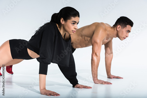 sportive multicultural woman and man doing push ups on white background