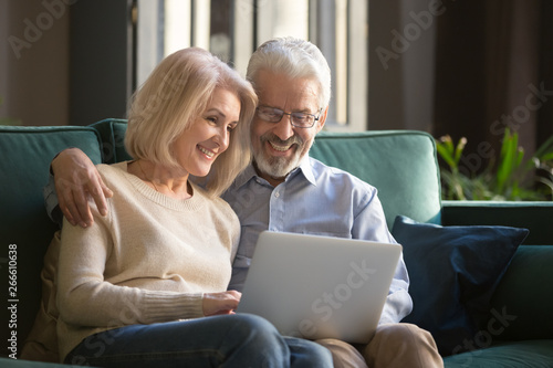 Smiling mature couple, wife and husband using laptop together at home