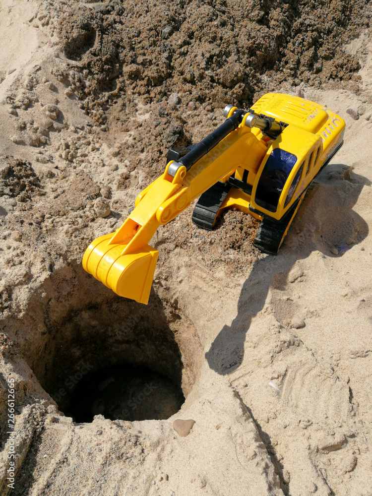 Plastic excavator child toy digging holes on the beach Plastic excavator child toy digging holes on the beach