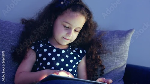 Cute Child Entertaining With Tablet. Little Girl Spending Leisure Time Playing Mobile Game in the and Crushes the Bright Screen With Her Hand. Concept of:Happy Childfood, Technology, Childen Play photo