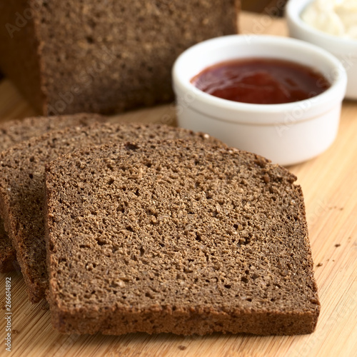 Slices of pumpernickel dark rye bread on cutting board with jam and cream cheese, photographed with natural light (Selective Focus, Focus in the middle of the slice) photo