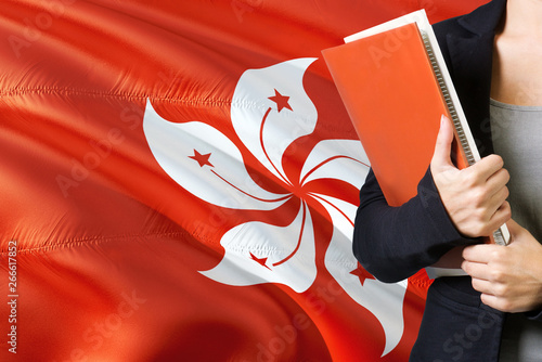 Learning language concept. Young woman standing with the Hong Kong flag in the background. Teacher holding books, orange blank book cover. photo