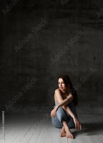 Sexy sensual beautiful woman posing naked in jeans sitting on a floor with free text space on dark old 