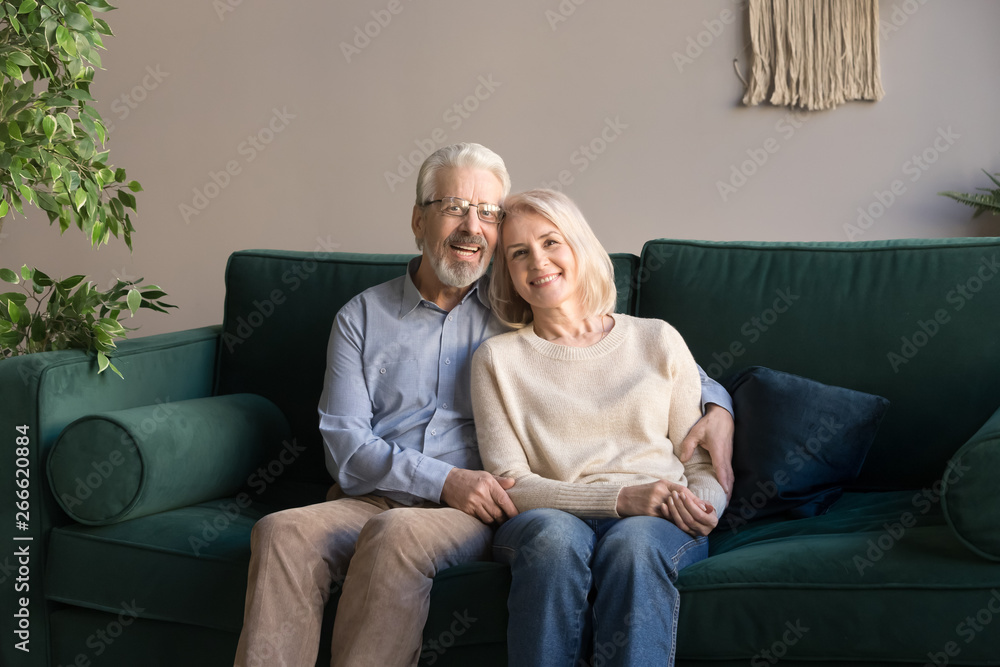 Portrait of hugging aged man and woman, family sitting on couch