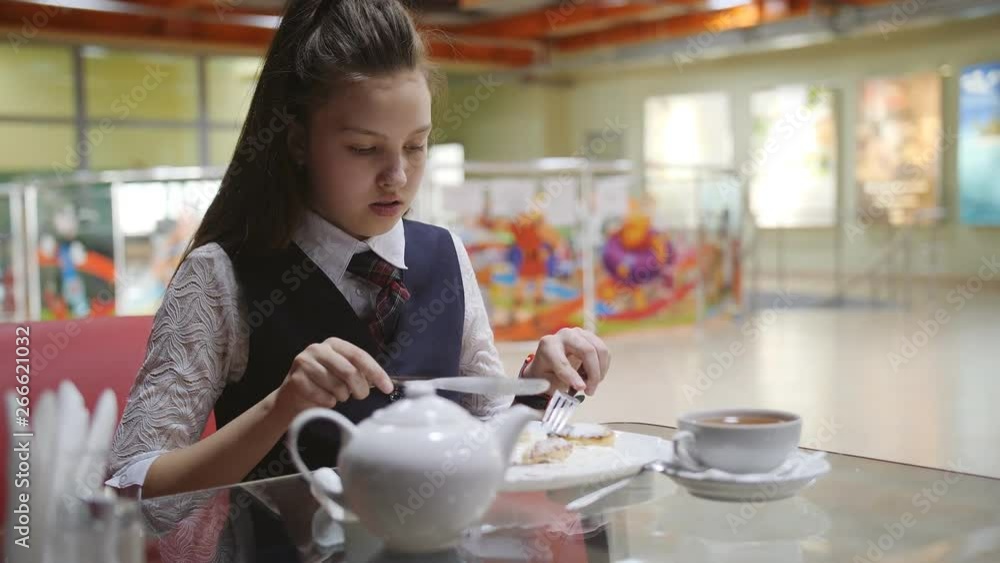 Lonely hungry schoolgirl eats in the school cafeteria during break. Lonely hungry schoolgirl eats in the school cafeteria during break.