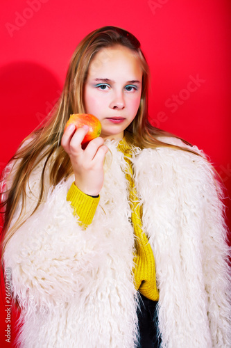 young pretty emitonal posing teenage girl on bright red background eating apple, happy smiling lifestyle people concept 