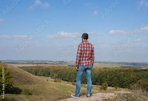 Young man standing on a hill enjoying scenery. Concept of travel and freedom.