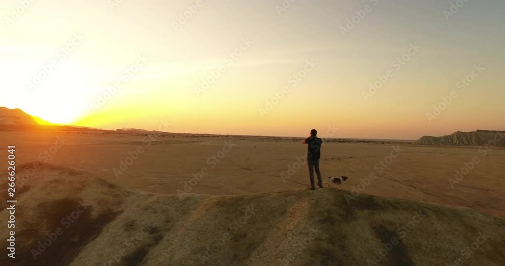 A rotating aerial shot of a man and his dog playing harmonica during sunset An aerial shot of a man and his puppy standing on top of a hill and playing harmonica long shadows golden hour A rotating aerial shot of a man and his dog playing harmonica during sunset An aerial shot of a man and his puppy standing on top of a hill and playing harmonica long shadows golden hour