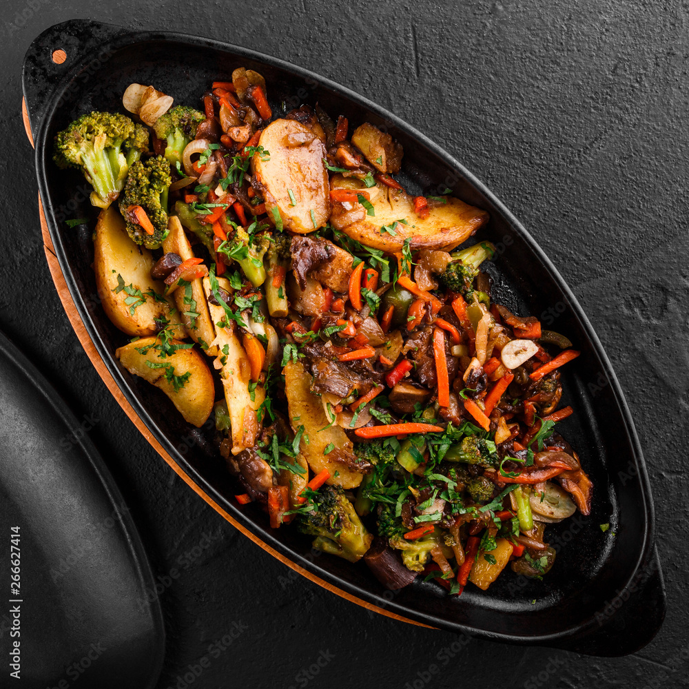 Baked vegetables, greens, potatoes, broccoli in pan on black stone background. Clean eating, healthy vegan food concept