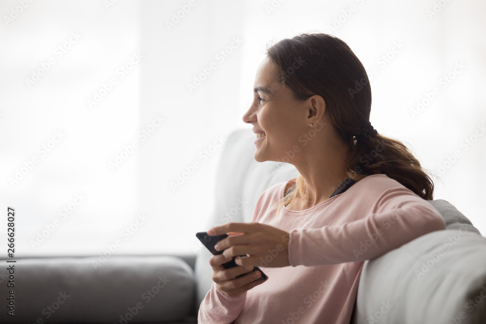 Side view of happy woman holding smartphone sitting on couch Side view of happy woman holding smartphone sitting on couch