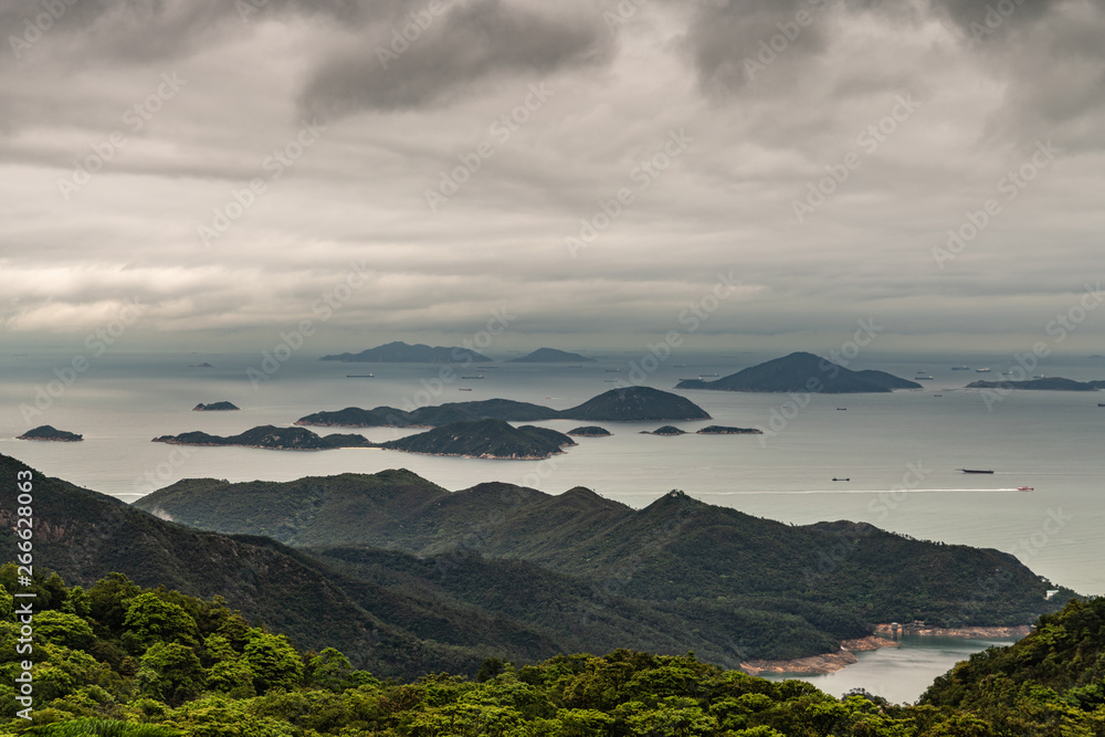 Obraz premium Hong Kong, China - March 7, 2019: Lantau Island. Pearl River estuary and South China Sea seen from Tian Tan Buddha platform. Green forested hill up front. Islands, boats, shorelines under heavy rainy