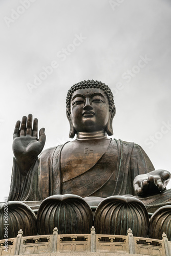 Hong Kong, China - March 7, 2019: Lantau Island. Frontal Facial view of Tian Tan Buddha statue from down under showing face, chest, lotus leaves and stone fence under silver sky.