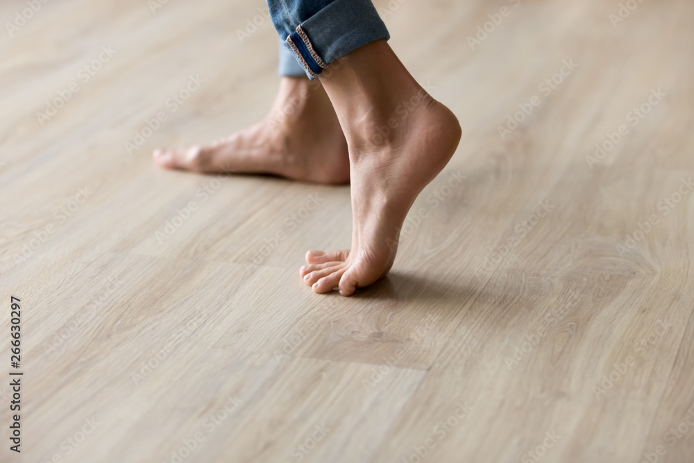 Side closeup view woman feet stands on warm wooden floor